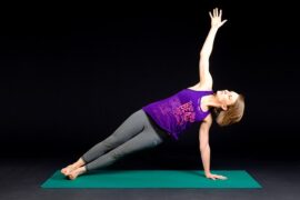 woman in workout gear doing a side plank stretch on a green exercise mat set against a plain black background