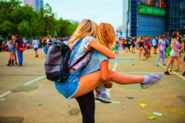 two blonde haired girls having fun at a summer festival. One is giving the other a piggy back.