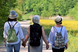 three women wth their backs to the camera going through the perimenopause together. They are holdng hands in support.